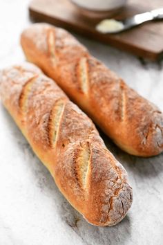 two loaves of bread sitting on top of a counter next to a knife and bowl