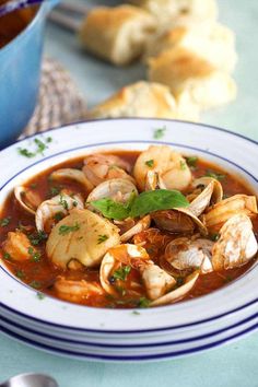 a bowl of soup with clams and bread in the background on a blue table cloth