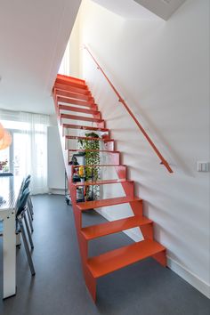 an orange stair case next to a table and chair in a room with white walls