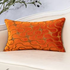 an orange and gold pillow on a white couch in front of a potted plant