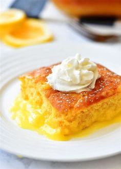 a piece of cake on a white plate with whipped cream and orange slices in the background