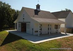 a large white barn with a clock tower on it's roof and an attached garage