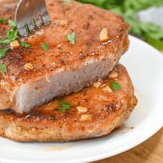 two pieces of meat on a white plate with a fork in it and garnished with parsley