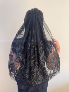 the back of a woman's head wearing a black veil with trees on it