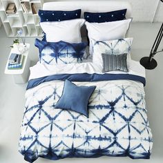 a bed with blue and white comforters, pillows and blankets on top of it