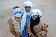 three young people with headscarves and scarves on their heads are standing in the dirt