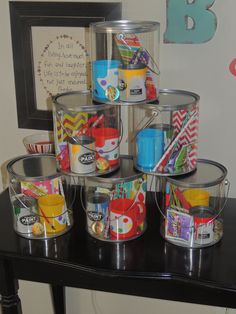 a black table topped with metal buckets filled with different types of paint and craft supplies