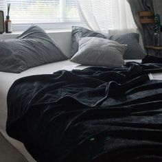 a bed with black blankets and pillows in front of a window