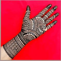 the hand is decorated with intricate designs on red and black background, which has been used as a hendi