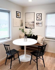 a white table and chairs in a room with wood flooring, framed pictures on the wall