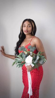 a woman in a red dress holding a bouquet of flowers and greenery with one hand