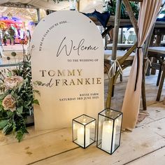 a welcome sign and two candles on a wooden table in front of a white banner