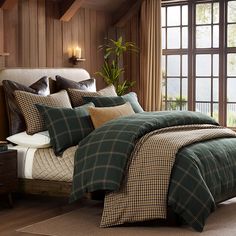 a bed with green plaid comforter and pillows in a room next to a window