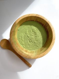 a wooden bowl filled with green powder next to a wooden spoon on a white surface