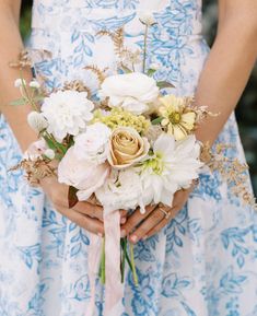 a woman holding a bouquet of flowers in her hands and wearing a blue floral dress