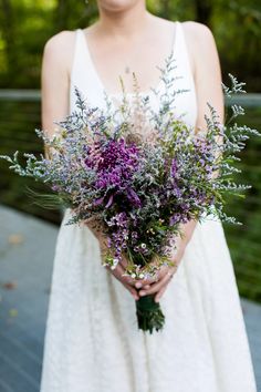 a woman in a white dress holding a bouquet of wildflowers and greenery