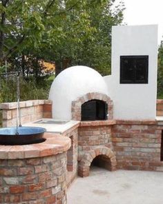 an outdoor pizza oven built into the side of a brick wall and surrounded by trees