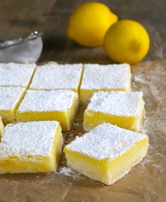 lemon bars are cut into squares on a cutting board with two lemons in the background