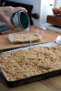 a person pours sugar into a baking pan on a wooden table with other food items