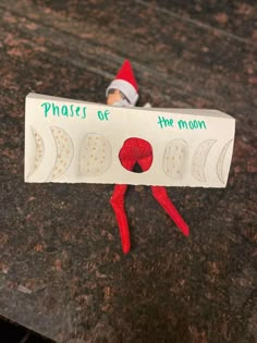 an elf is sitting on top of a paper sign that says phases of the moon