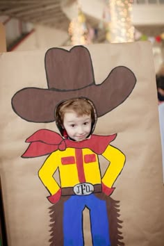 a young boy wearing a cowboy hat and holding a paper bag with the image of a man on it