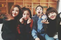 four young women posing for the camera in front of a bookshelf