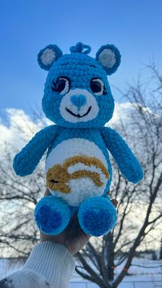 a hand holding up a crocheted blue and white teddy bear in the snow