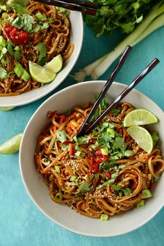 two white bowls filled with noodles and garnished with cilantro, limes, and chili