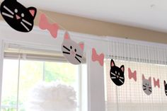 cat paper garland hanging from the ceiling in front of a window with curtains behind it