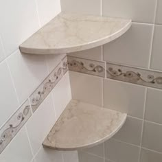 two shelves in the corner of a white tiled shower stall with marbled tiles on the walls