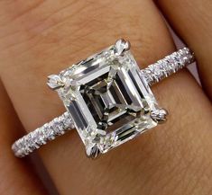 a woman's engagement ring with an emerald cut diamond and pave diamonds on the band