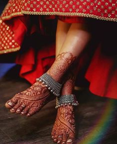 the feet and ankles of a woman with henna tattoos on their feet, sitting in front of a rainbow