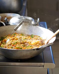 a wok filled with noodles and vegetables on top of a stove