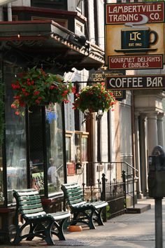 two green benches sitting on the side of a street next to a parking meter with flowers hanging from it