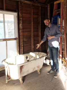 a man standing next to a bath tub in a room with wooden floors and walls