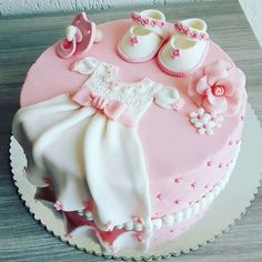 a cake decorated with pink and white baby's clothes on top of a wooden table