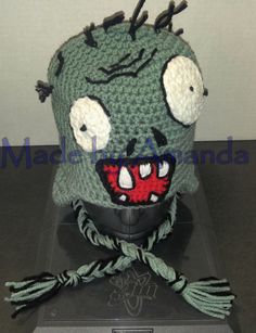 a crocheted green hat with white eyes and hair on top of a table