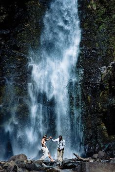 two people standing in front of a waterfall