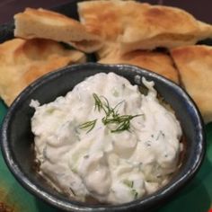 a bowl filled with whipped cream next to pita bread on a green tablecloth