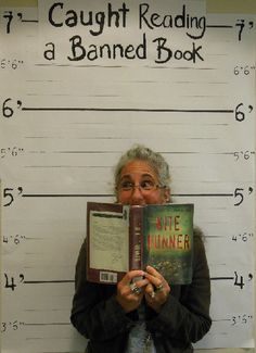 a woman holding a book in front of a mugshot sign that says caught reading a banned book