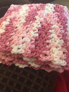 a pink and white crocheted blanket sitting on top of a couch