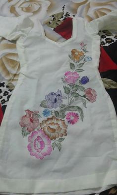 a white dress with flowers on it sitting on top of a quilted table cloth