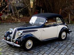 an old black and white car parked on a cobblestone street