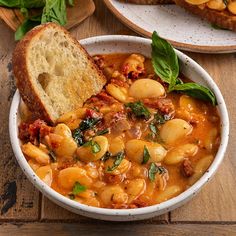 a bowl of soup with bread on the side and basil sprigs in it