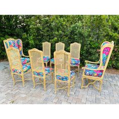 a set of seven chairs and a table on a brick patio with trees in the background