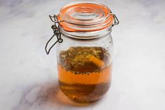 a glass jar filled with liquid sitting on top of a white counter next to an orange lid