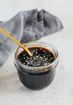 a jar filled with sesame seed sauce on top of a white tablecloth next to a wooden spoon