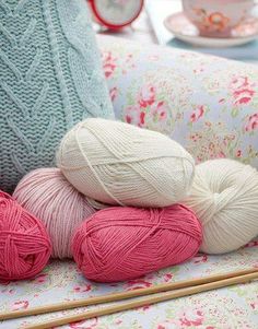 balls of yarn and knitting needles sitting on a chair next to a cup with tea in it