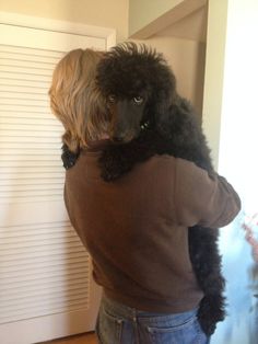 a woman holding a black poodle in her arms while standing next to a door