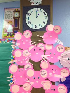 a bulletin board with pink paper cutouts on it and a clock in the background